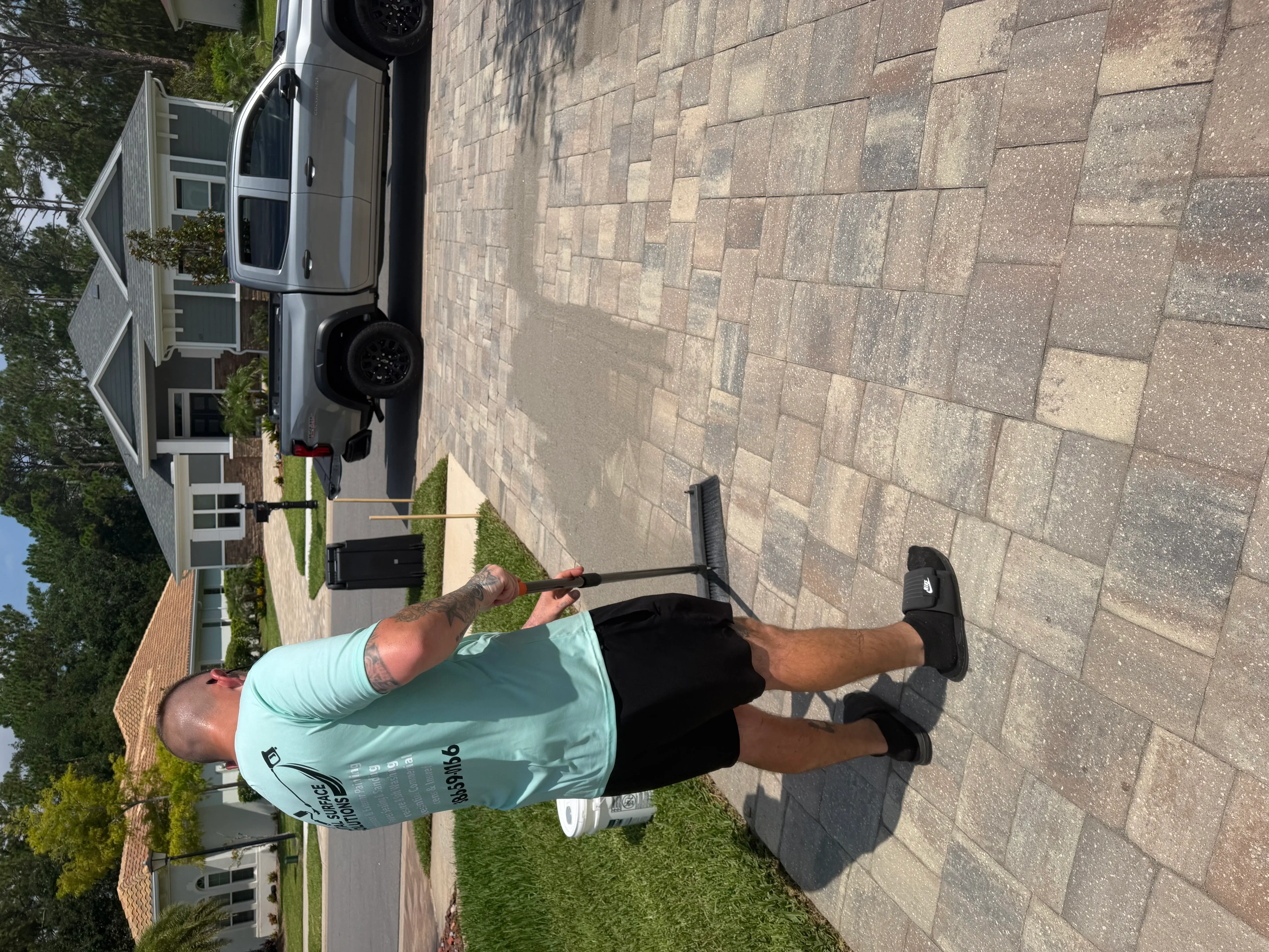 Technician pressure washing multi-colored concrete paver driveway at residential home