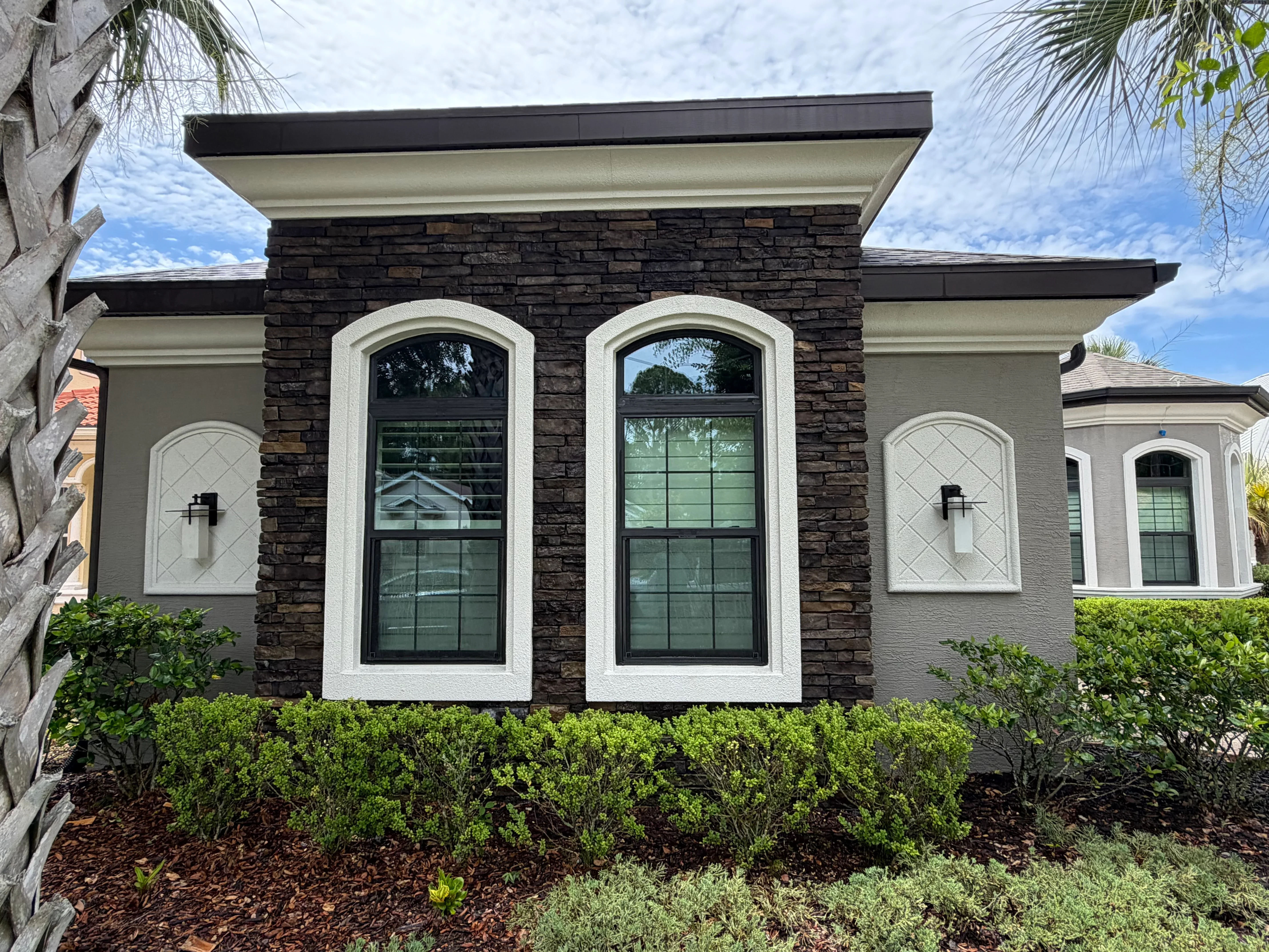 Modern home with dark stone facade, white-trimmed arched windows, and clean gray brick exterior