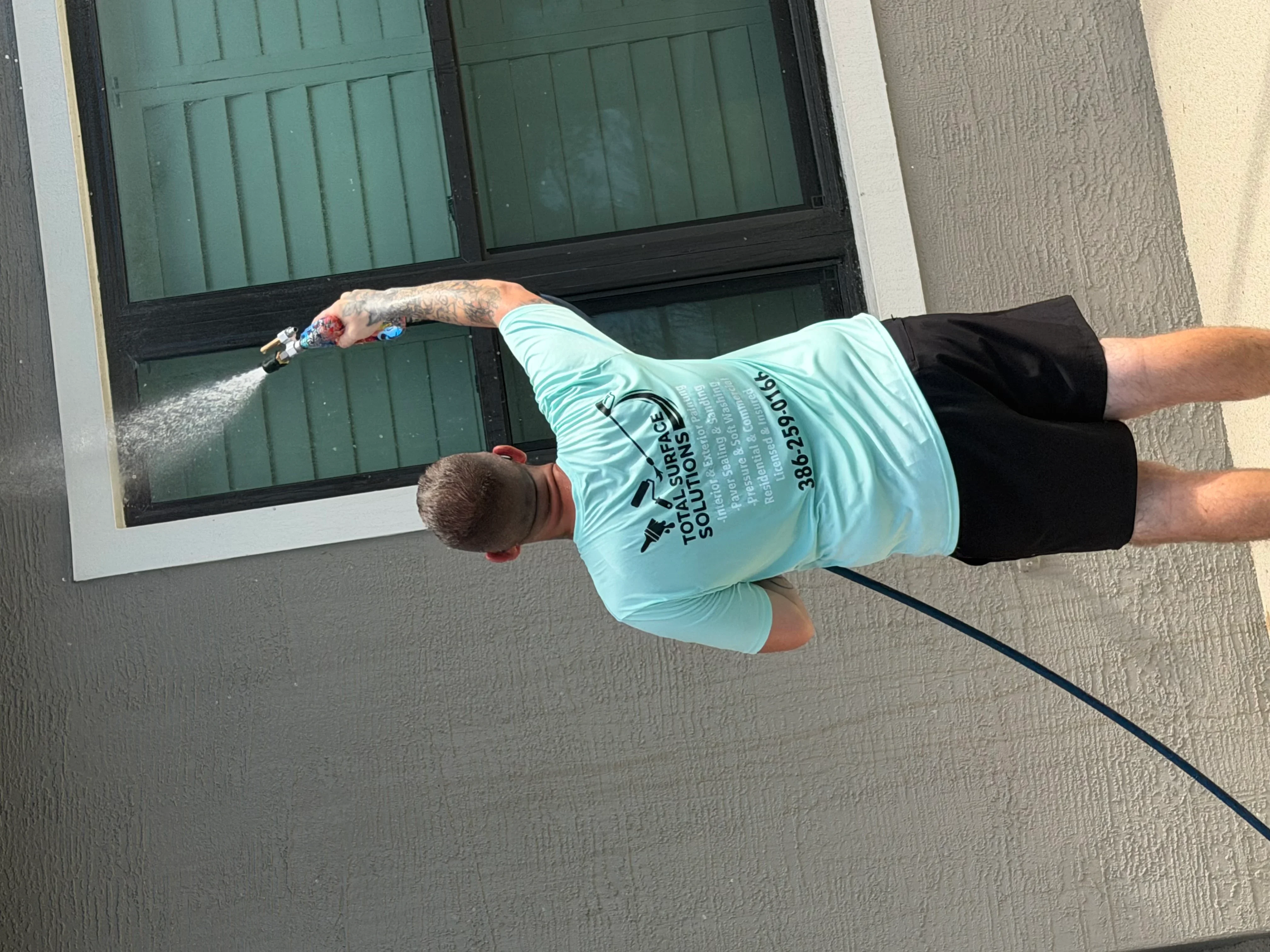 Technician pressure washing green garage door and tan stucco exterior wall