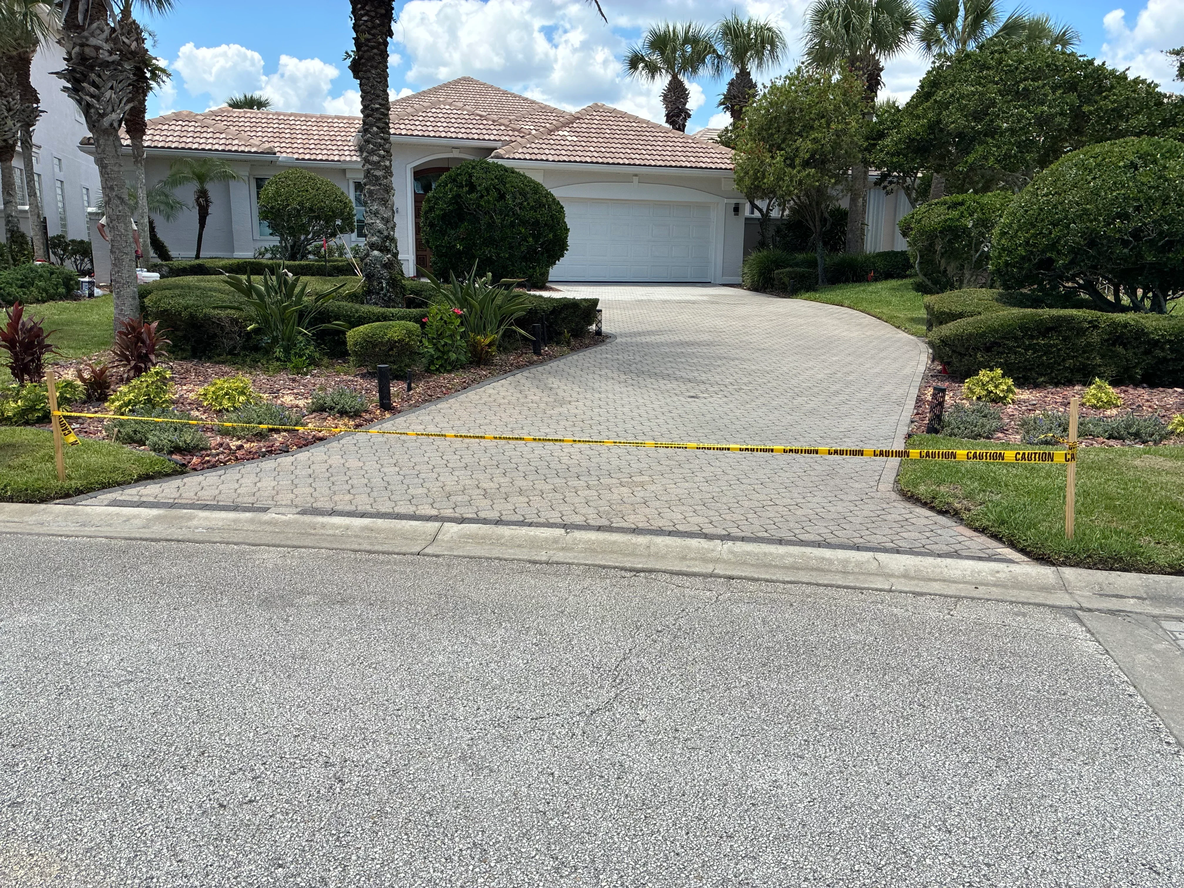Sealed paver driveway with curved design in front of white Florida home with tile roof