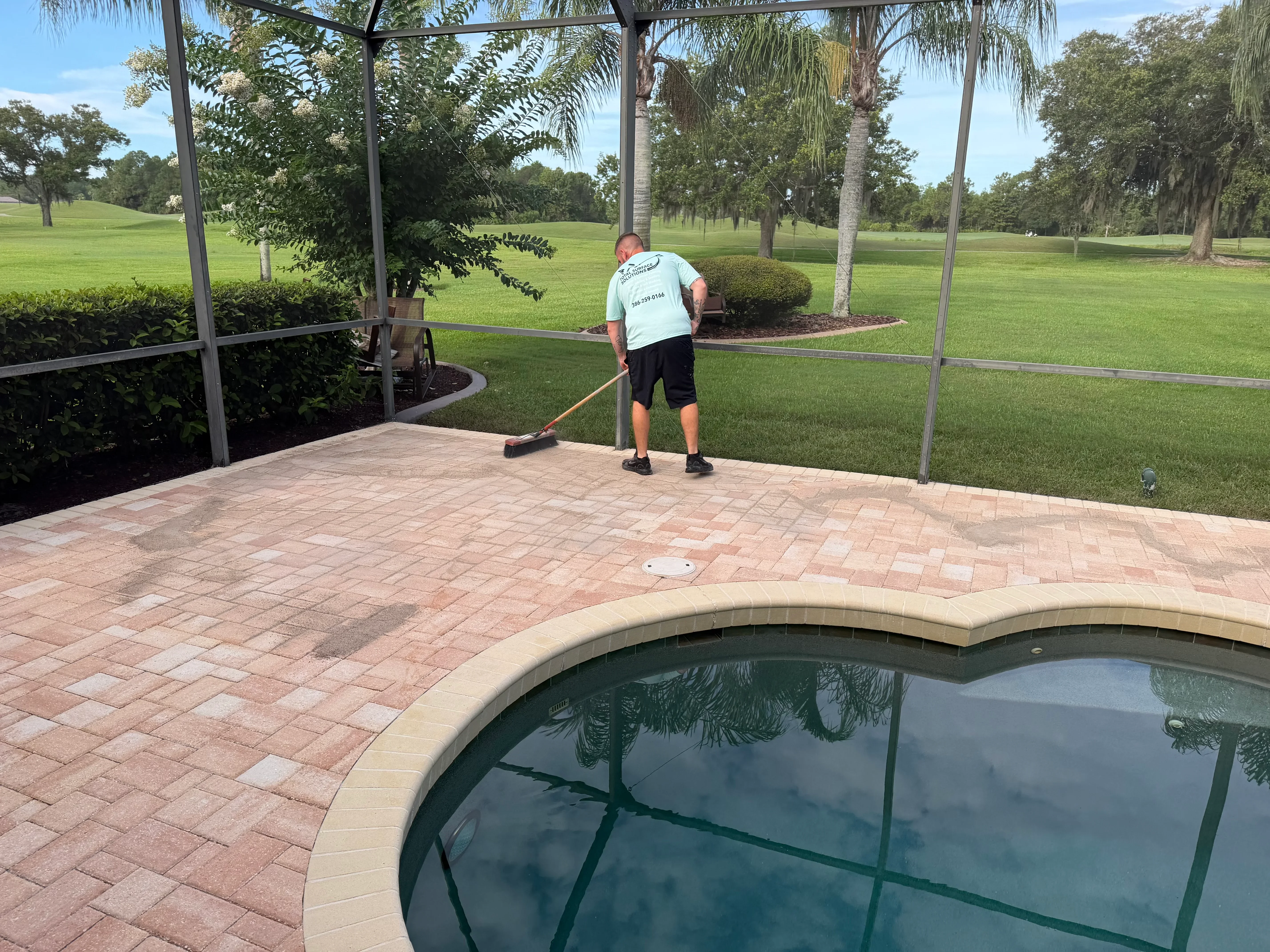 Worker pressure washing clay brick pavers around residential pool deck in Palm Coast