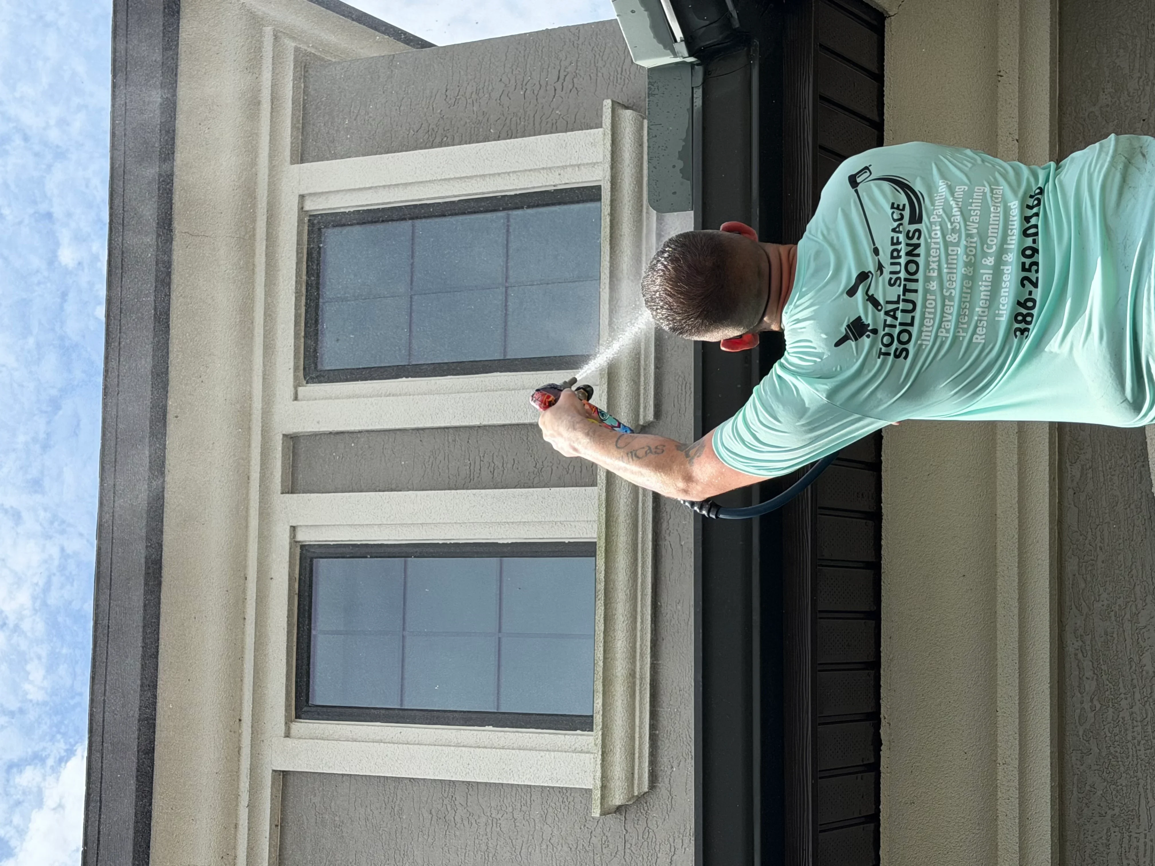 Technician pressure washing residential home exterior and window frames in Palm Coast