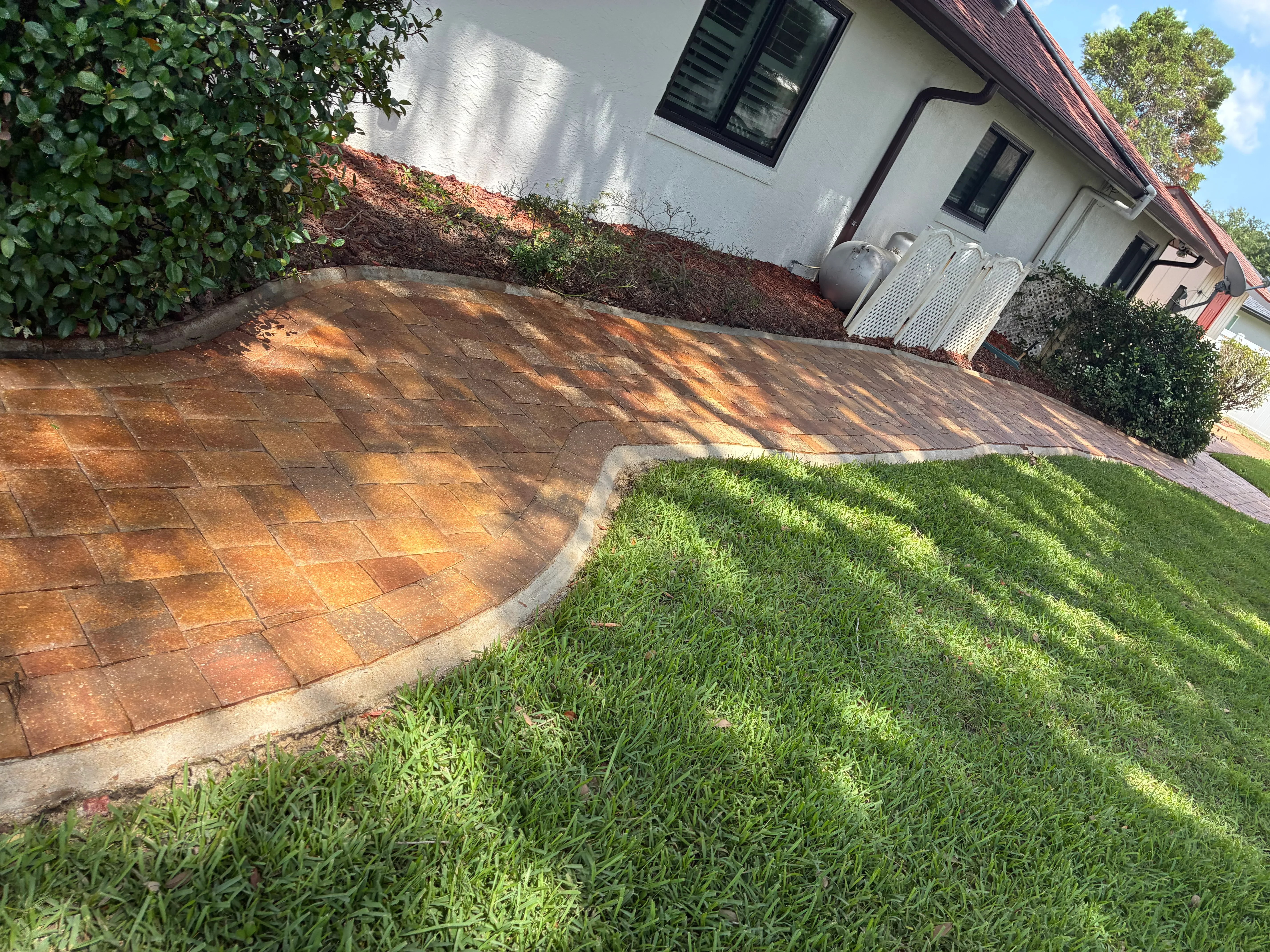 Clean clay brick paver patio with concrete edging next to manicured lawn and landscaping