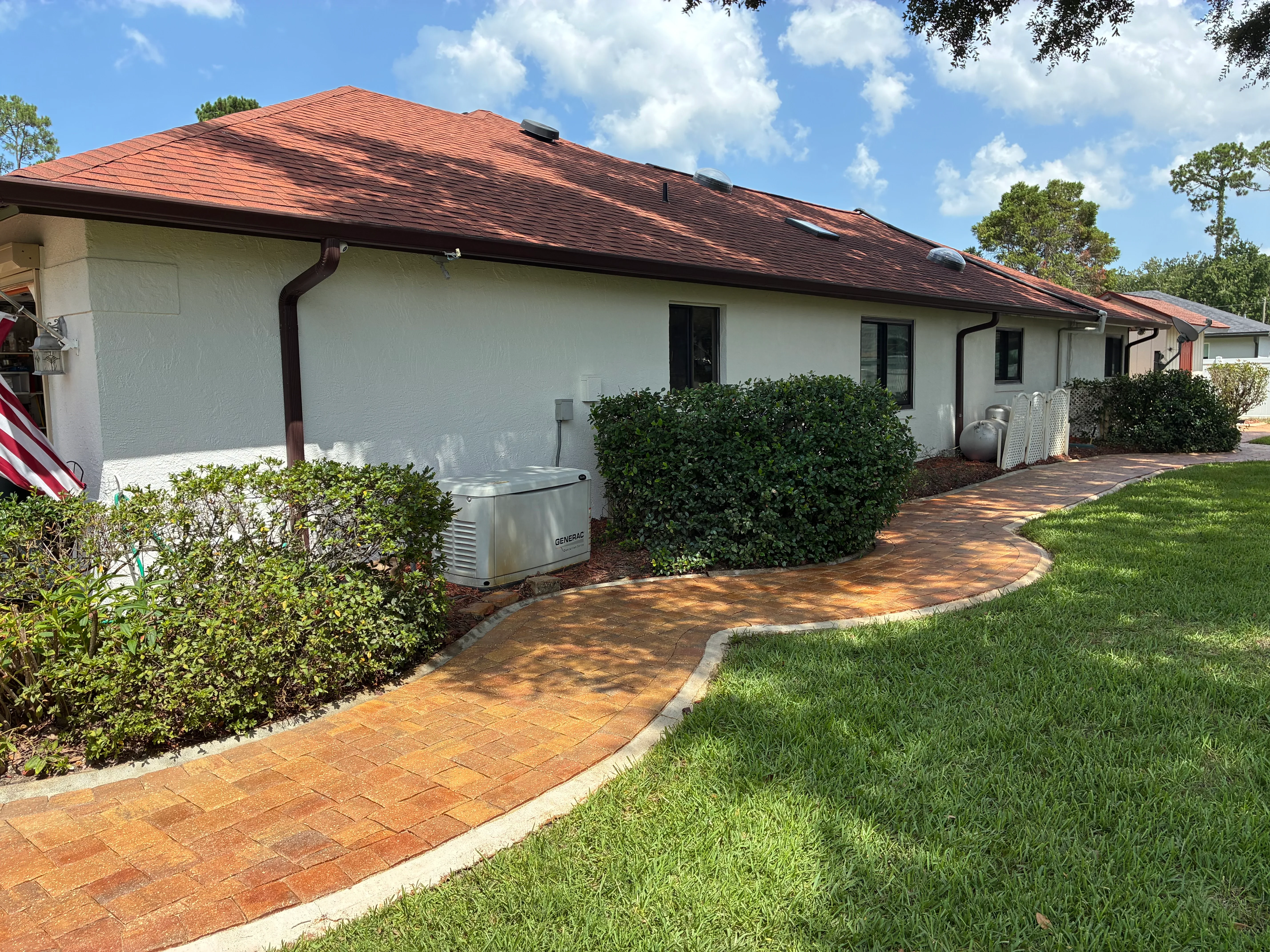 Clean white stucco home with red clay tile roof and freshly cleaned brick paver walkway