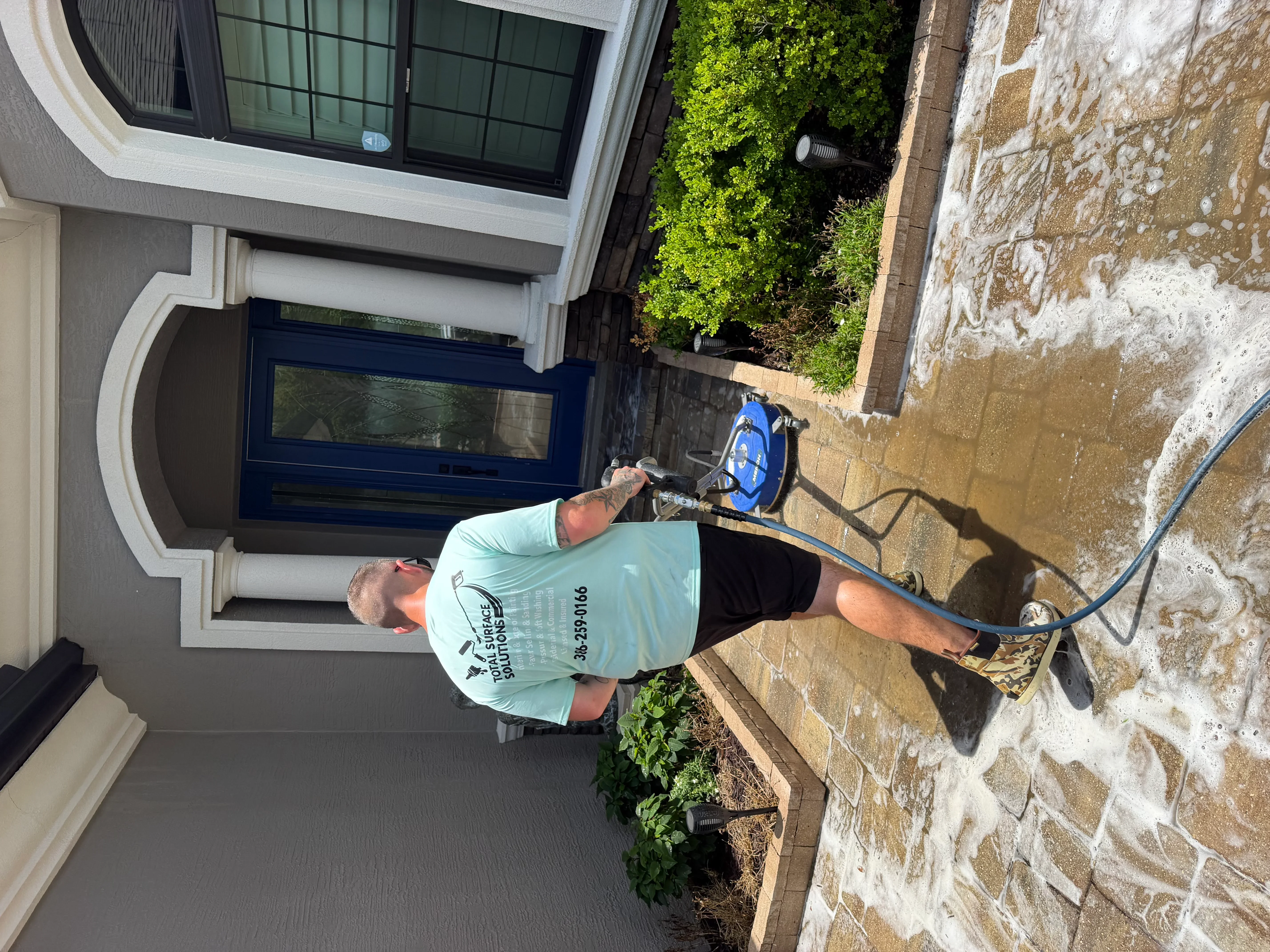 Technician pressure washing residential driveway and brick foundation in Palm Coast