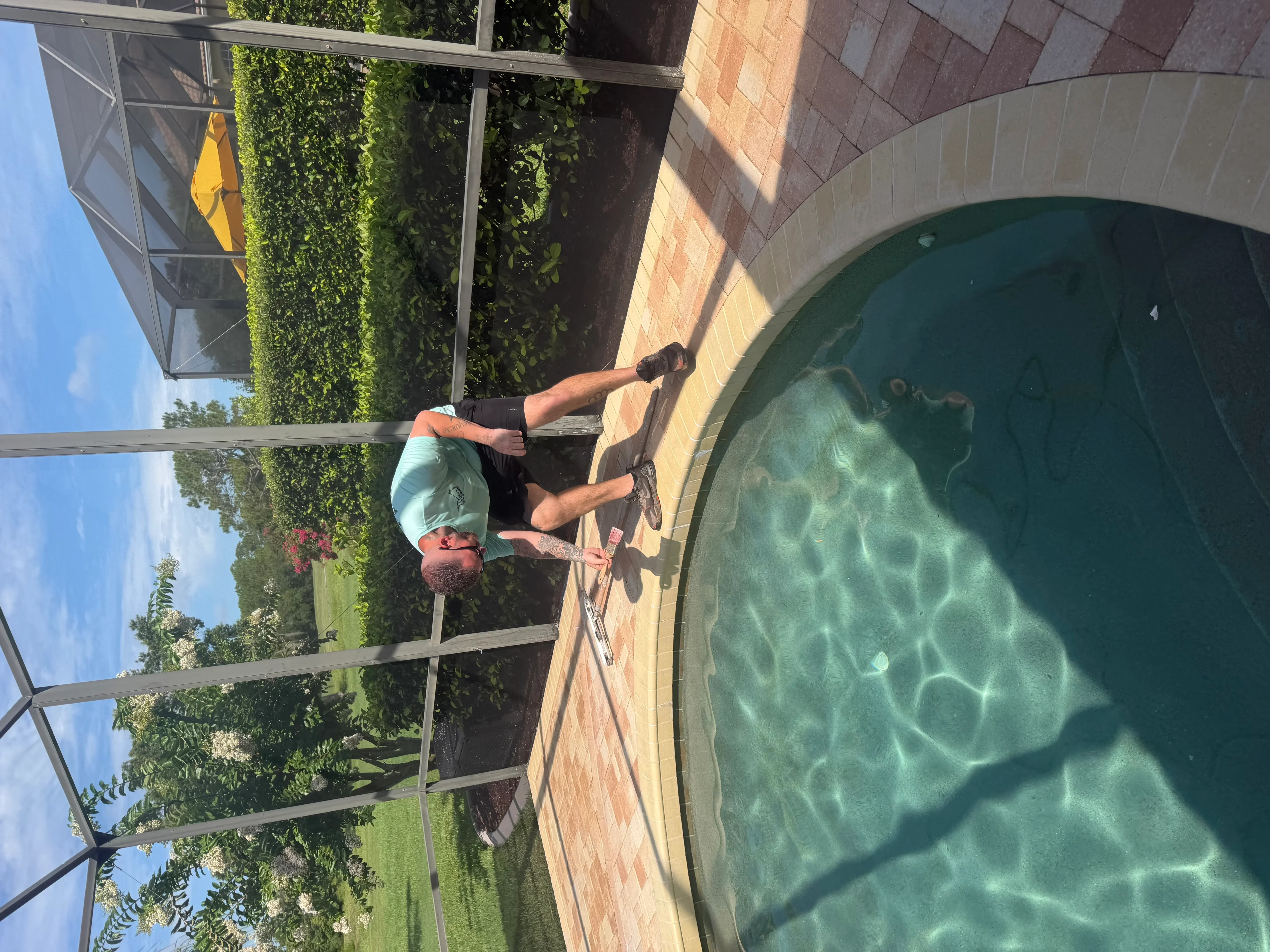 Technician cleaning and maintaining in-ground pool with brick surround in Palm Coast