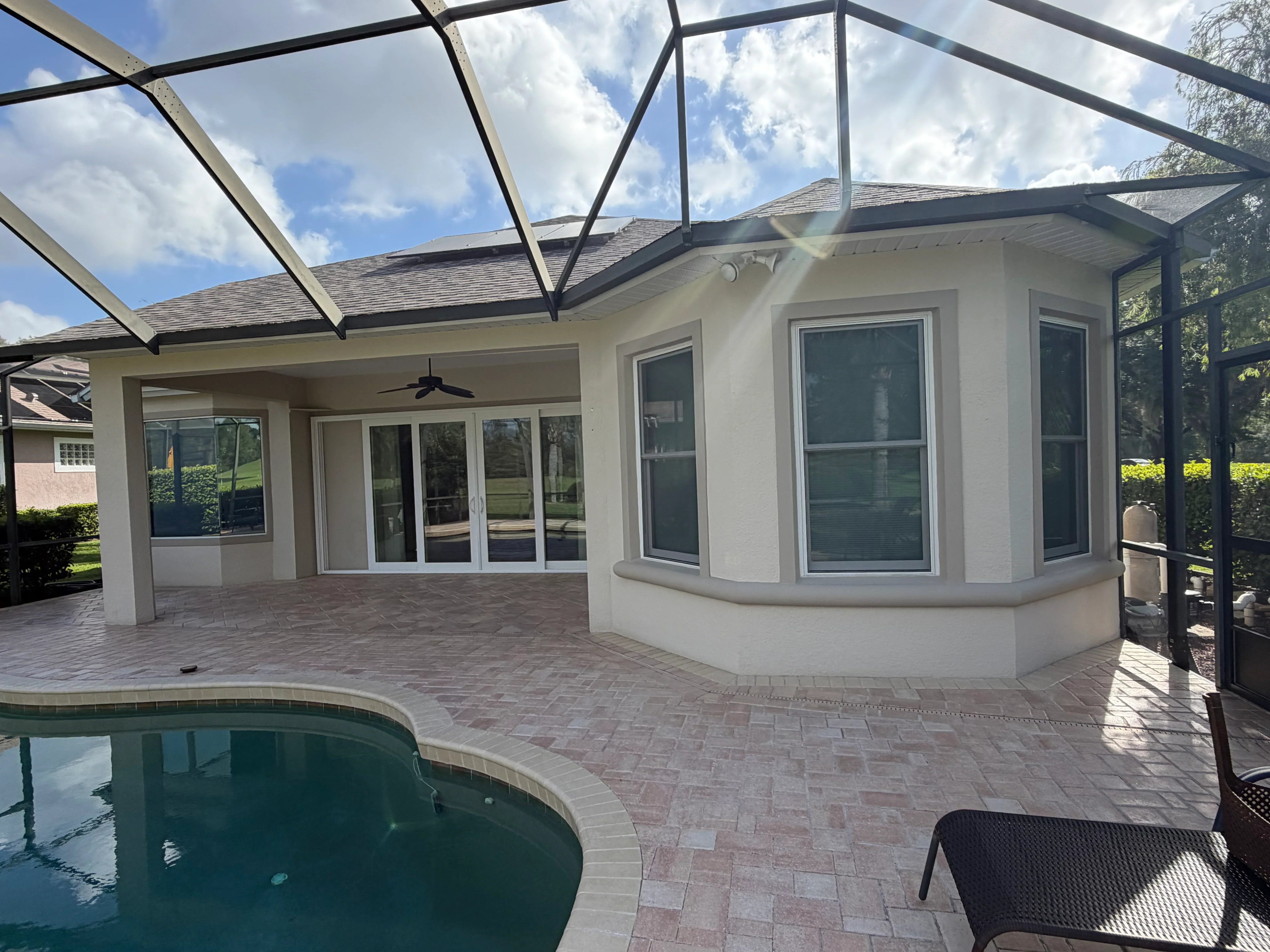 Clean pool deck with herringbone pavers, screened lanai, and glass roof enclosure