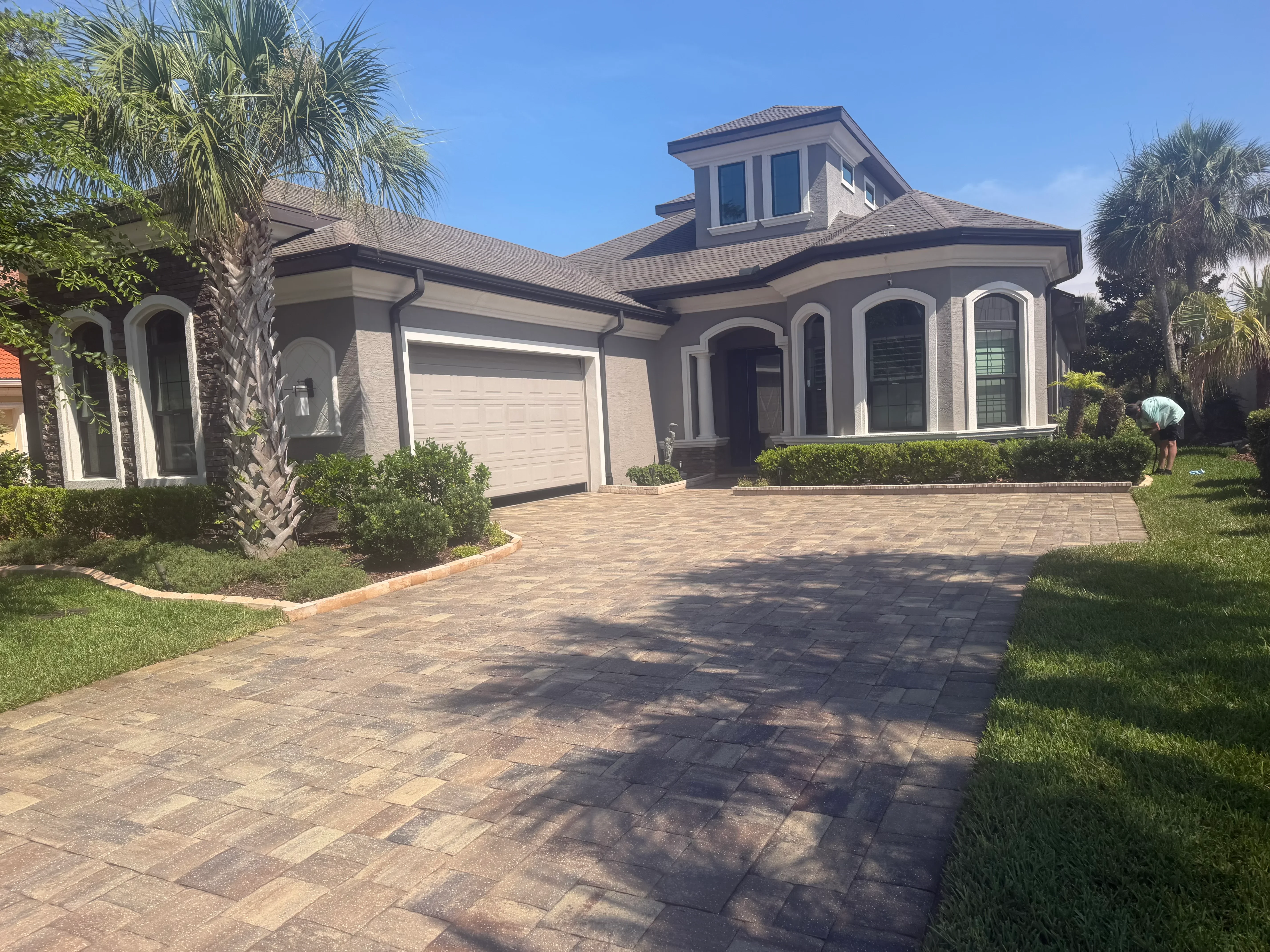 Clean stucco home with freshly pressure-washed paver driveway and manicured landscaping