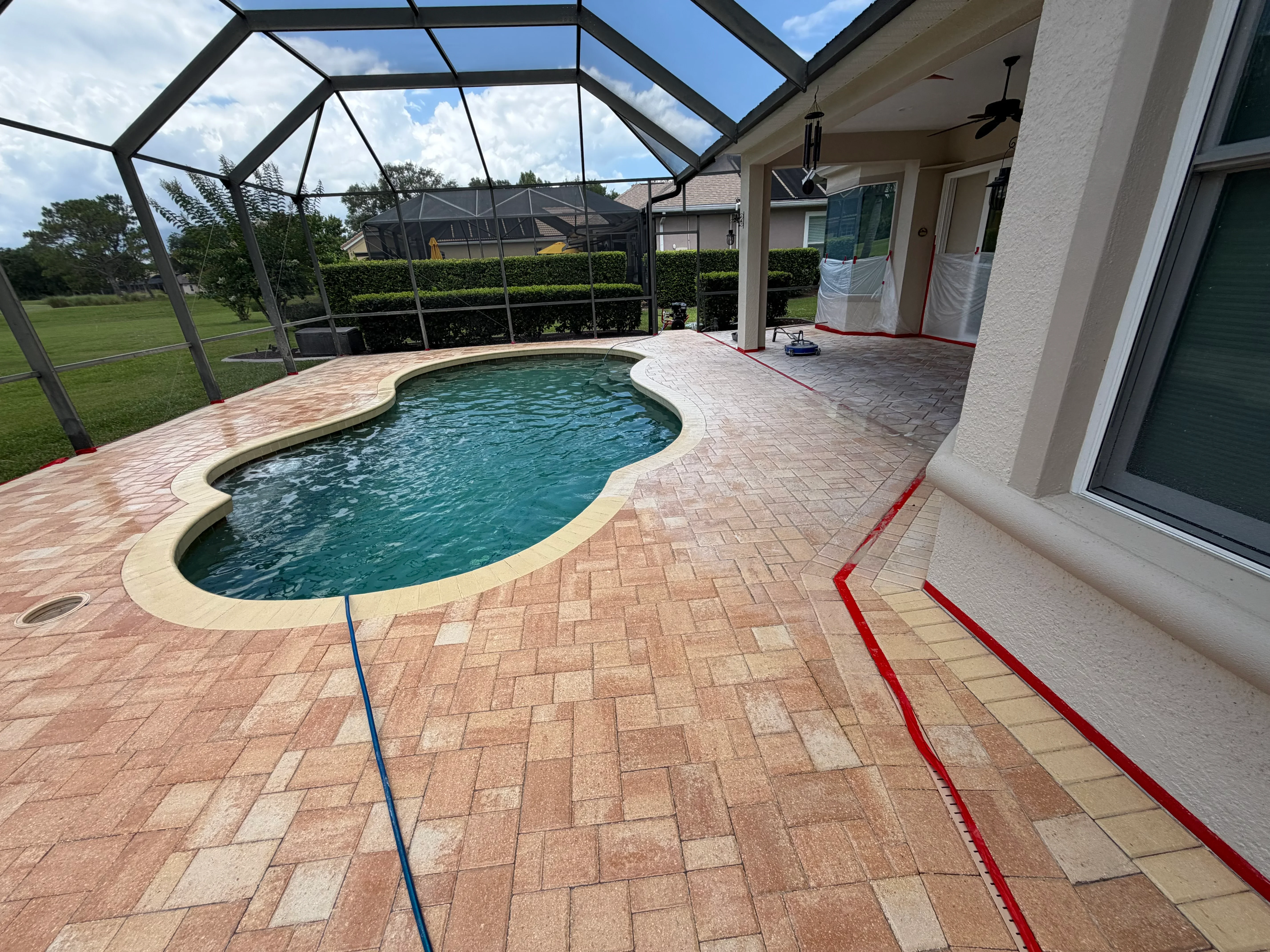 Clean clay brick paver pool deck with turquoise pool and black screened enclosure