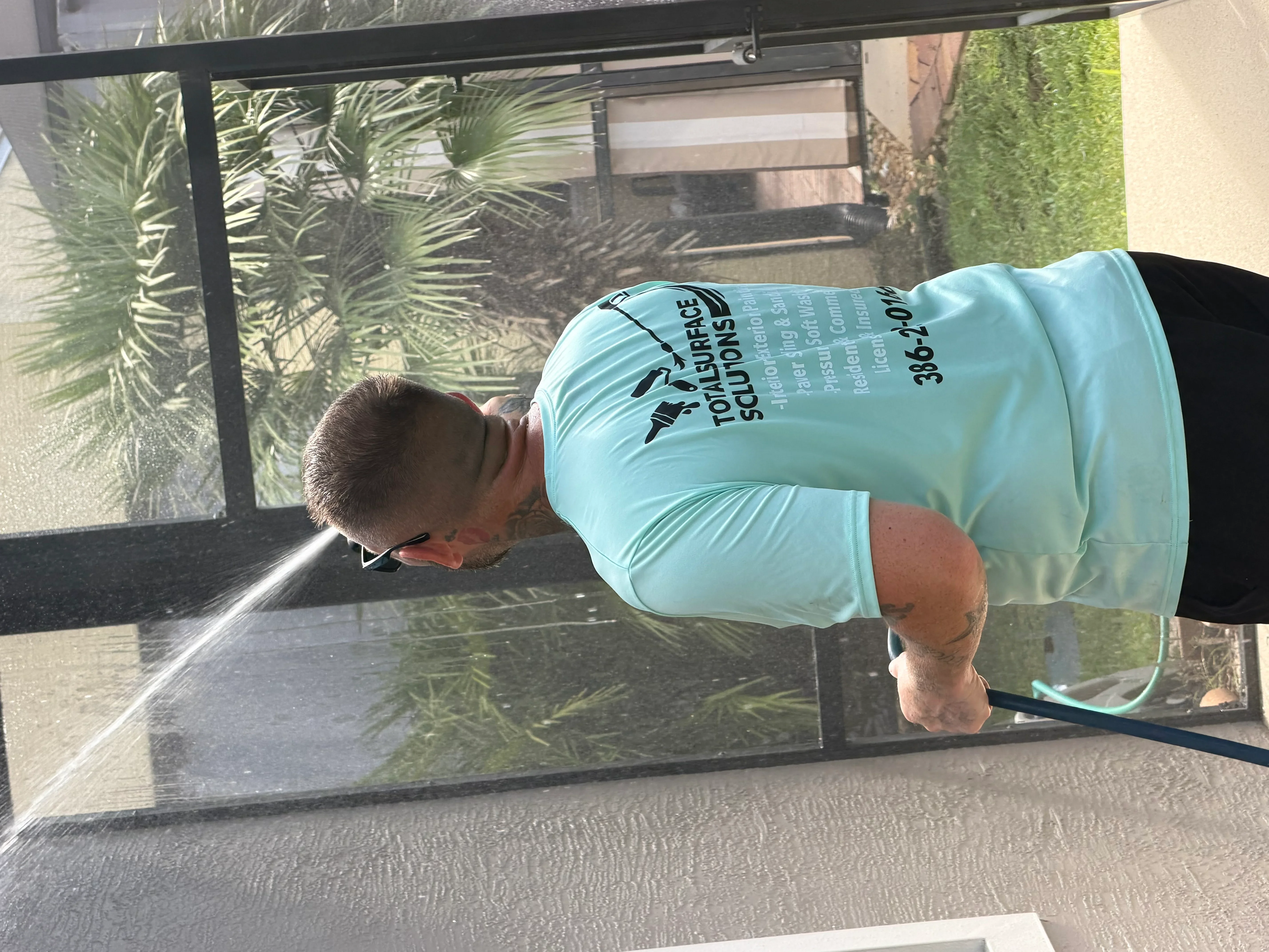 Technician pressure washing residential window frame and glass with precision spray technique