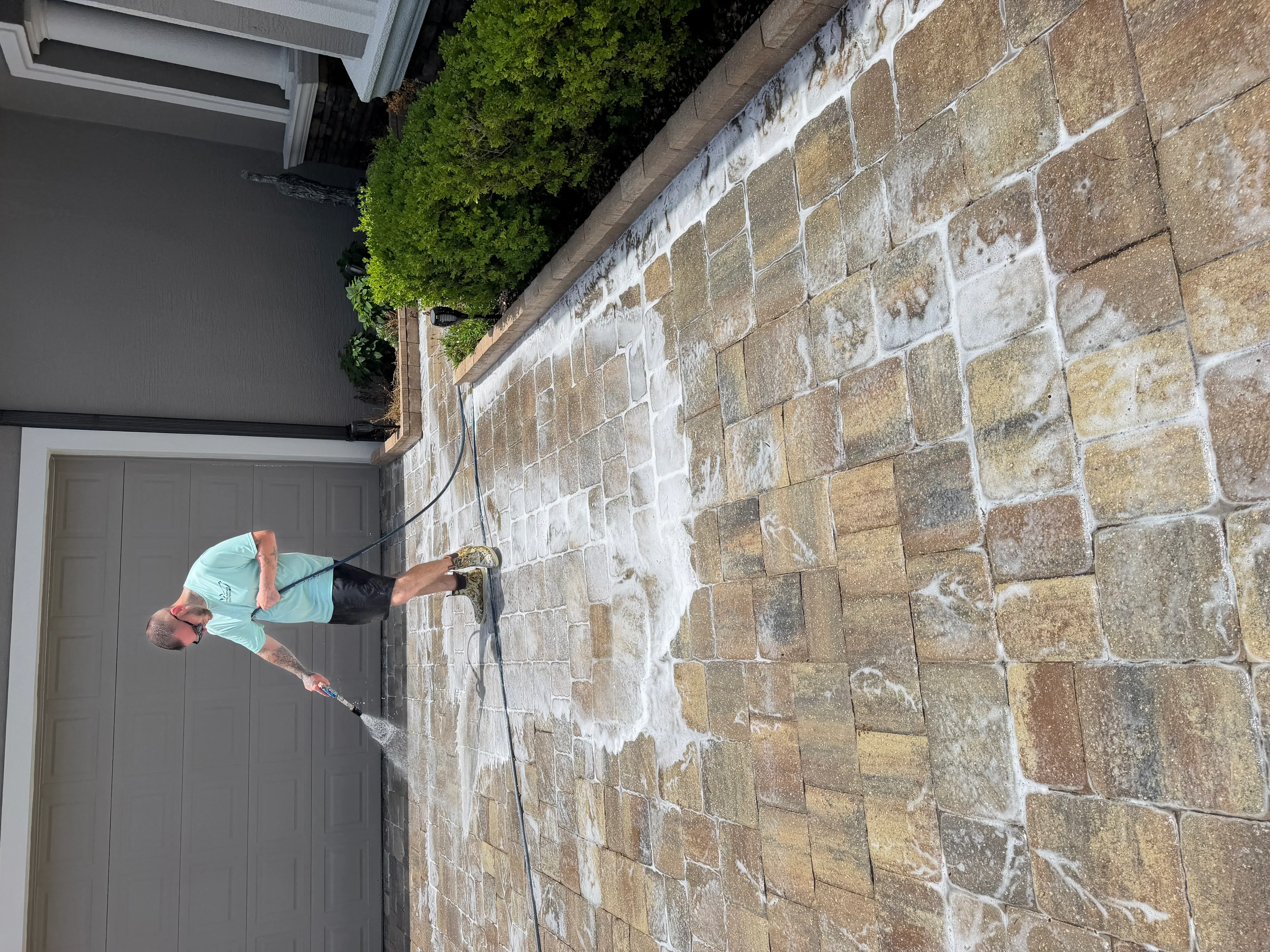 Technician pressure washing stone masonry wall with visible cleaning results