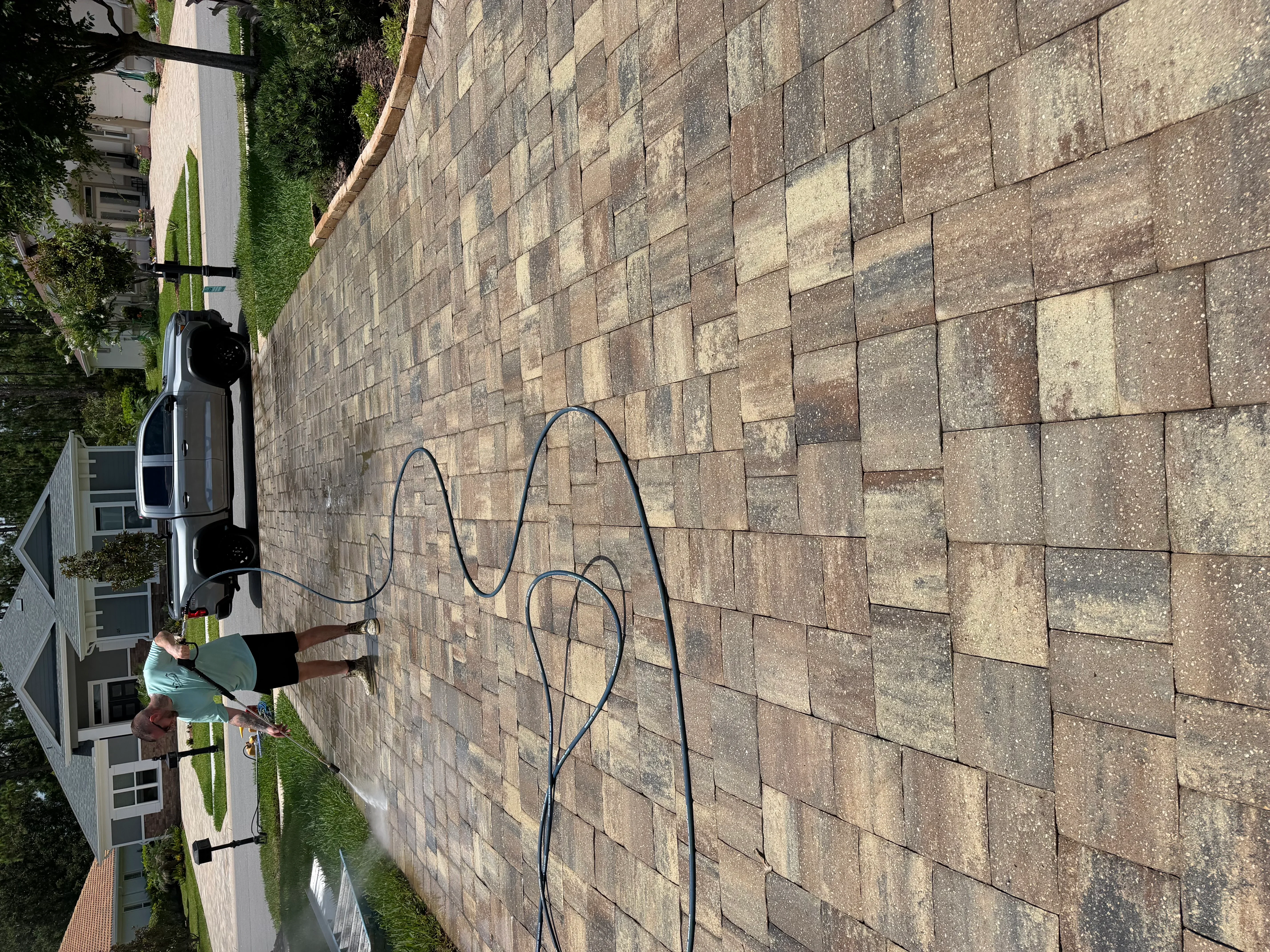 Technician pressure washing large residential paver driveway with multi-colored concrete pavers